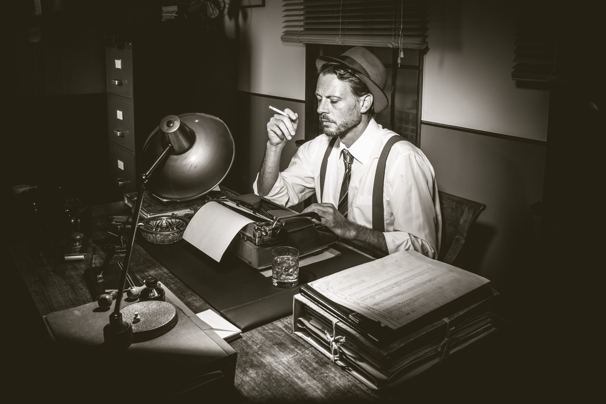 Man sitting at a desk, wearing a hat and smoking a cigarette