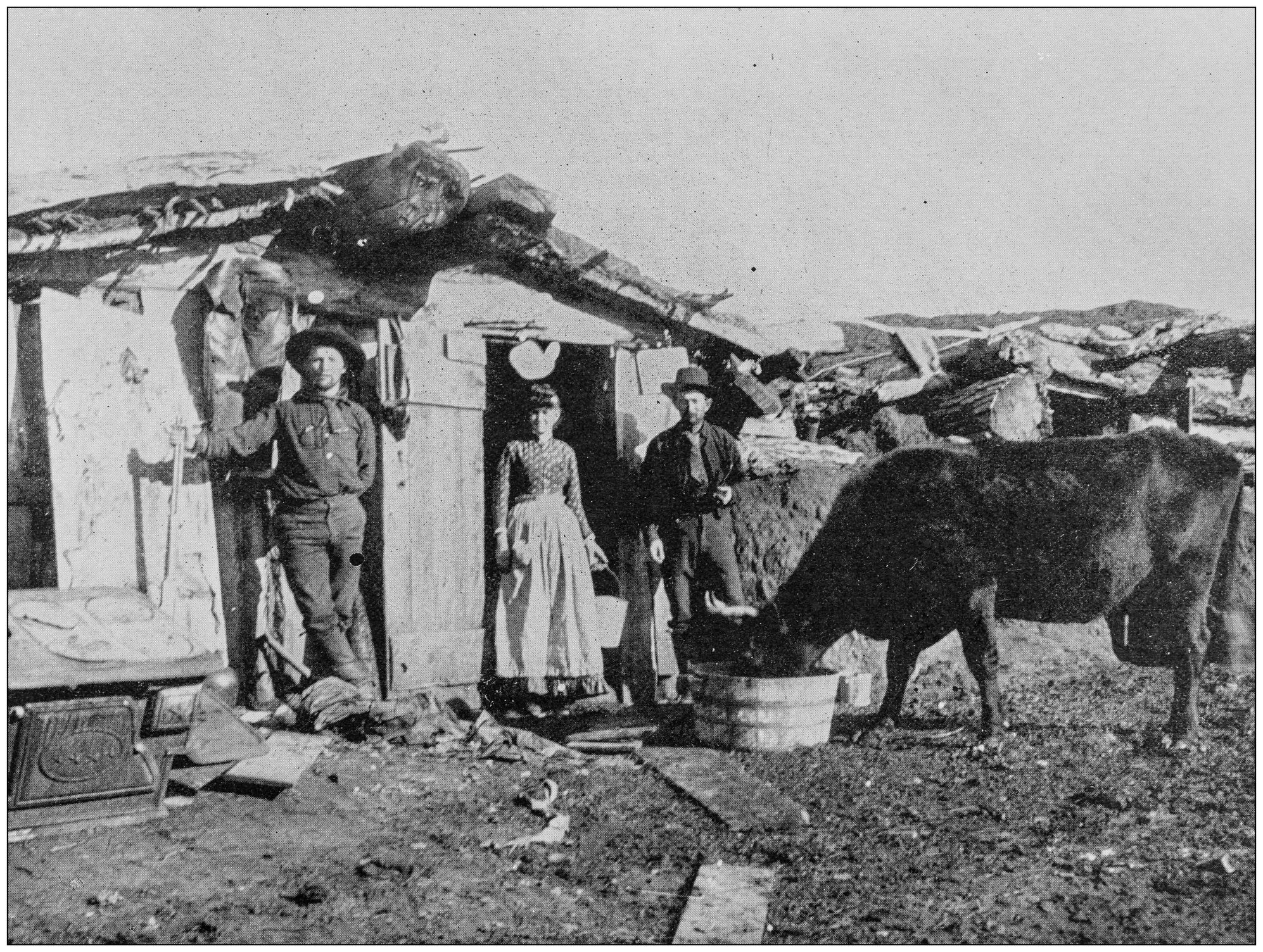Group of people standing in front of a hut, with a cow standing nearby