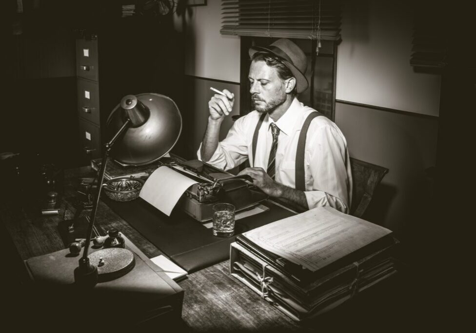 Man sitting at a desk, wearing a hat and smoking a cigarette