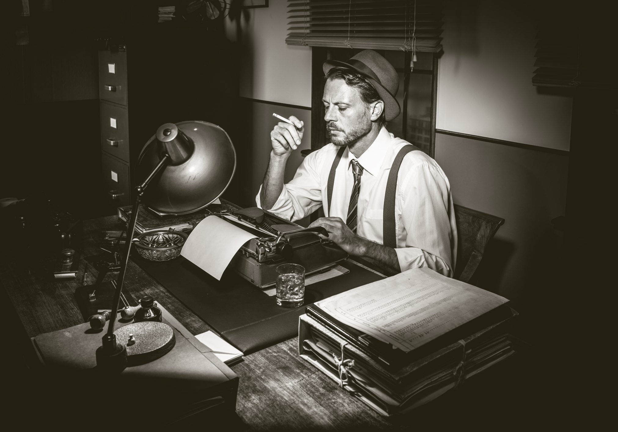 Man sitting at a desk, wearing a hat and smoking a cigarette