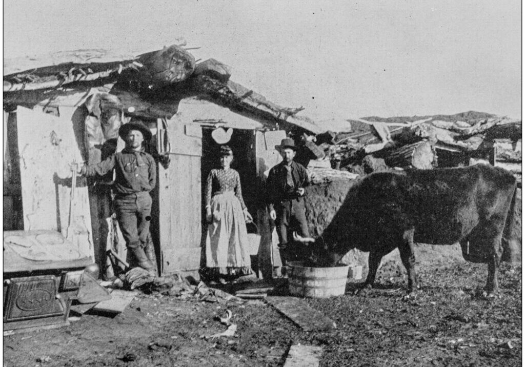 Group of people standing in front of a hut, with a cow standing nearby