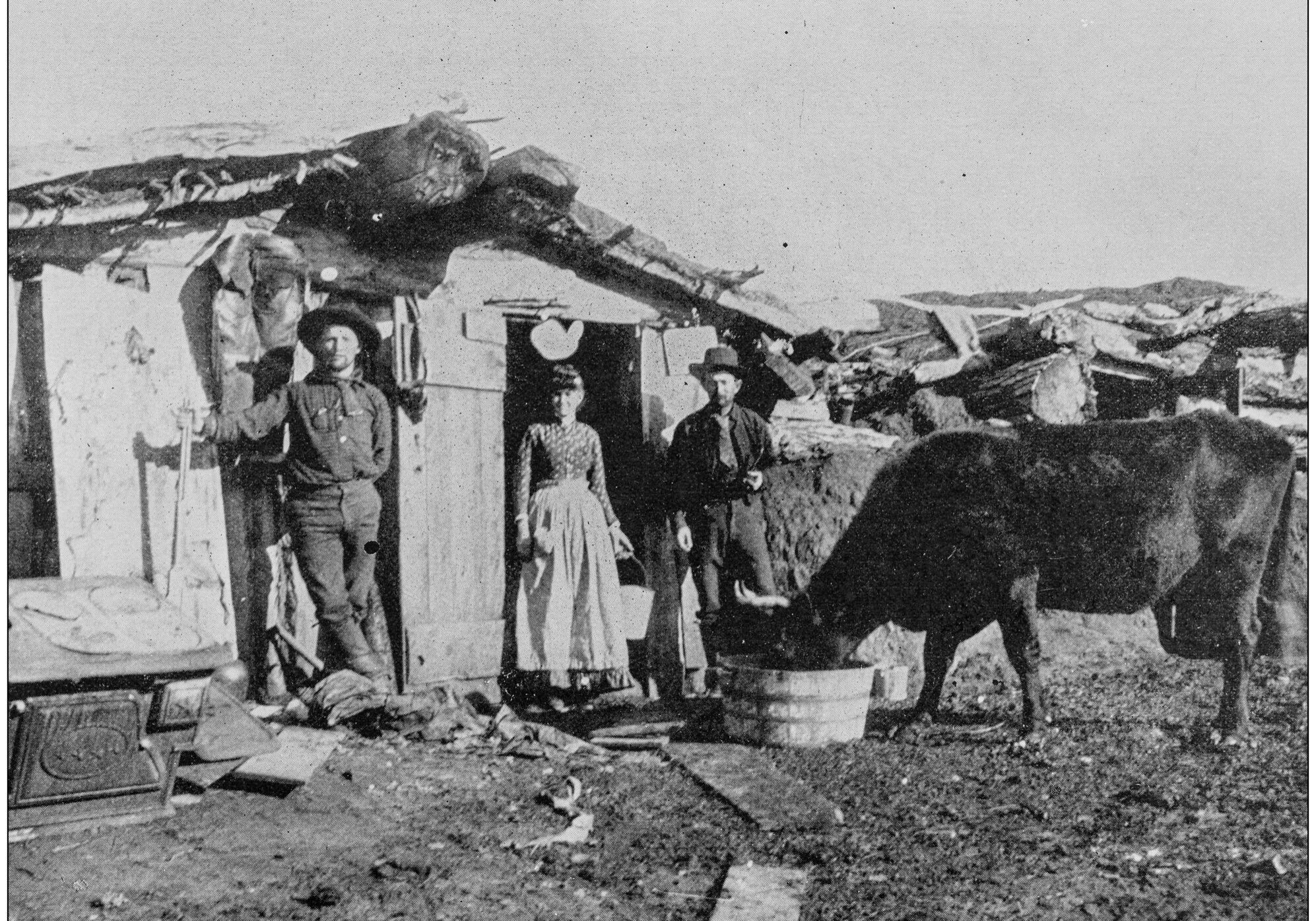Group of people standing in front of a hut, with a cow standing nearby